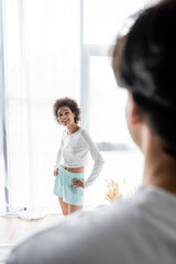 Obraz premium happy african american woman standing with hands on hips while looking at blurred boyfriend