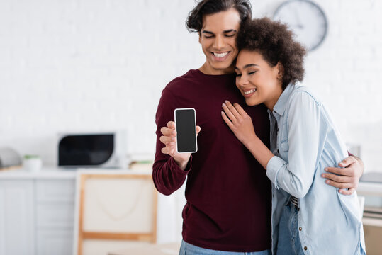 happy man holding smartphone with blank screen near smiling african american girlfriend