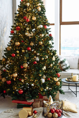 Christmas tree with red and gold balls and gold garland lights in a bright room.