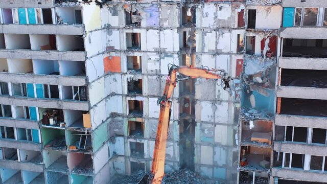 Excavator grabber reaches high to dismantle the walls of an old building. Parts of concrete and heavy dust falling down. Construction excavators are clearing the ruins of an old building.