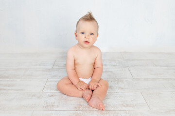 cute baby boy in diapers on a white background with a hairstyle and big blue eyes smiles