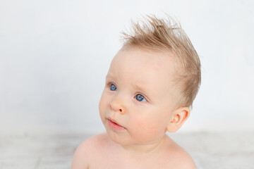 portrait of a cute baby boy on a white background with a hairstyle and big blue eyes smiling