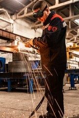 A plant worker is welding metal with a welding machine in a protective mask and overalls against...