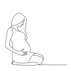Young pregnant woman in a dress sits on her knees and holds her hands on her belly with her baby.