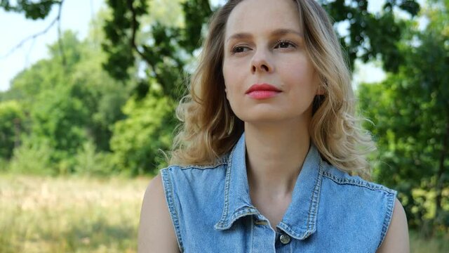Portrait of a young beautiful blonde woman in a denim suit against a background of green foliage. Summer relaxation