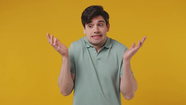 Fun confused awkward confused preoccupied shy shamed young man 20s years old wear blue t-shirt look camera spreading hands say oops ouch oh omg i am so sorry isolated on plain yellow background studio