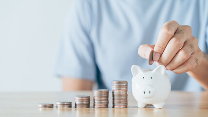 Closeup of man hand putting money coin into piggy bank for saving money. saving money and financial...