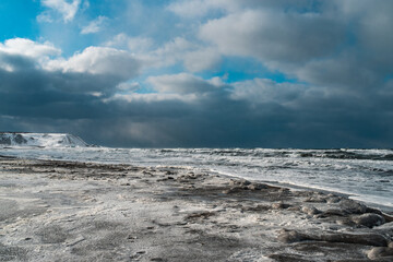 Winter landscape with frozen sea and icy beach. Storm and snow weather. Dramatic seascape.