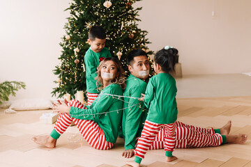 The concept of Christmas. Cheerful children in green pajamas have fun tied up their parents with a...