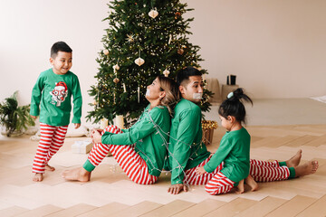 The concept of Christmas. Cheerful children in green pajamas have fun tied up their parents with a...