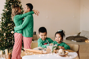 A happy mixed Asian family with two children in green pajamas cook cookies together and prepare for...