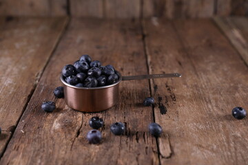 Blueberries in a small measuring glass on a wooden background