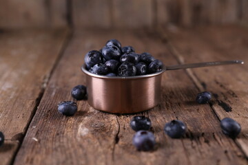 Blueberries in a small measuring glass on a wooden background