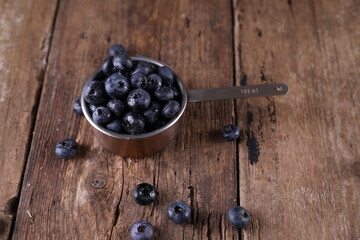 Blueberries in a small measuring glass on a wooden background