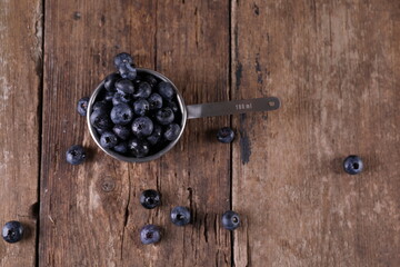 Obraz na płótnie Canvas Blueberries in a small measuring glass on a wooden background