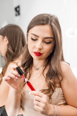 Makeup artist applies red lipstick . Beautiful woman face. Hand of make-up master, painting lips of young beauty model girl . Make up in process