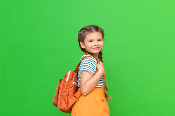 A little girl with a school bag on a green isolated background. Copy space.