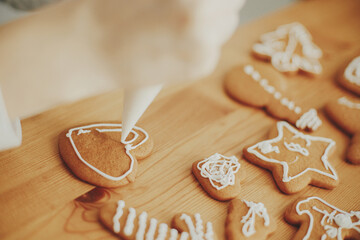 Decorating christmas gingerbread cookies with icing on wooden table close up. Hands decorating...