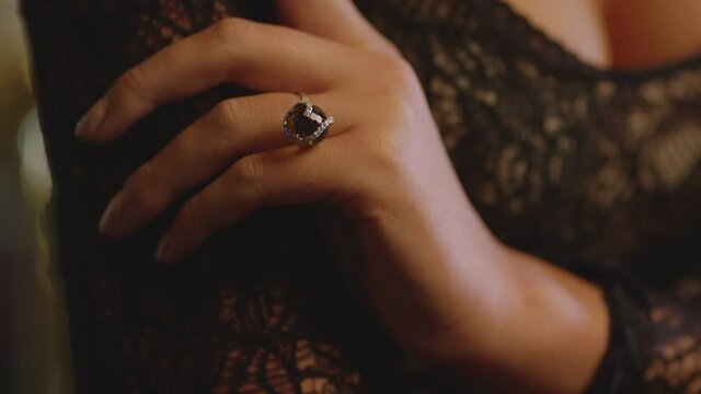 Close up hand of elegant woman in lace or guipure black dress wearing expensive luxury ring with precious stone and showing it . Model presenting jewelry of famous designer in fashion show . 