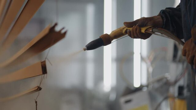 A close-up of Molar sprays paint on steel profiles in a respirator mask and protective suit in slow motion. Production and painting studio. Powder coating