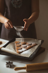 Baker sprinkles icing sugar from a sieve on Christmas gingerbread, close-up.