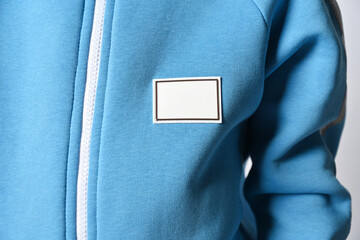 Closeup of kid in blue jacket with zipper and blank rectangular patch for copy paste over light background. Chest, sleeve