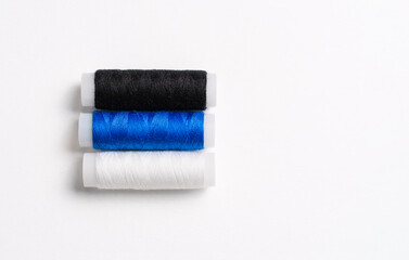 Three spools of thread for sewing are stacked in the form of the flag of Estonia on a white background. There is a free empty space.