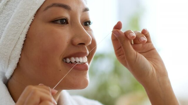 Dental hygiene concept. Close up portrait of young asian woman cleaning her teeth with tooth floss, caring about smile