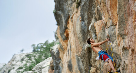 Fit and focused athletic man climbing challenging route on high vertical cliff. Muscular well built, toned strong body