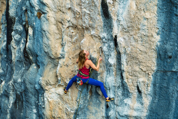 Athletic woman climbing on high beautiful rock cliff, feeling determined on challenge route