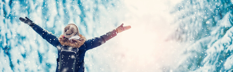 Happy woman with hands up standing in the snowy forest in snowfall.