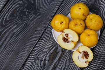 Naklejka na ściany i meble Quince fruits on a plate. The yellow fruit is cut, the seeds are visible. Plate on black pine boards. Close-up shot.