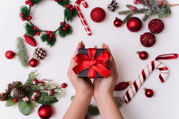 New Year or Christmas composition on a white background hands with a gift box, with a red ribbon with fir branches, toys, copy space for congratulations. Give a gift