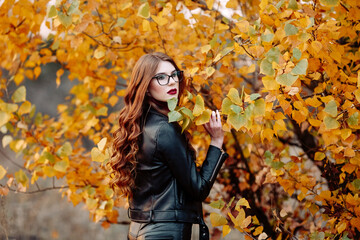 Fototapeta na wymiar portrait of a beautiful young woman, wearing stylish glasses, looking at the camera. Happy, confident, smart young woman in autumn foliage