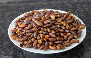 Roasted baru (Dipteryx alata) chestnuts, rotating on the white plate with many chestnuts falling on the scene. Typical Brazilian chestnut, very nutritious and healthy