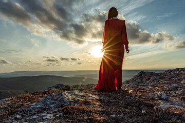 Rise of the mystic. sunset over the clouds with a girl in a long red dress. Stands on the mountain with a magical view.