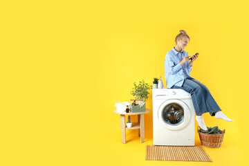 Concept of housework with washing machine and girl on yellow background - obrazy, fototapety, plakaty
