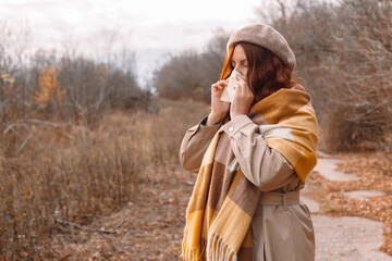 Young female with handkerchief. Sick girl has runny nose in a cold autumn day.