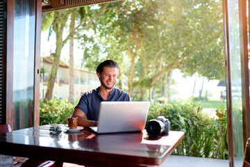Freelance concept. Professional photographer. Young  bearded man using laptop while sitting on summer terrace.