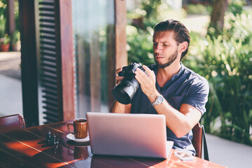 Freelance concept. Professional photographer. Young  bearded man using laptop while sitting on summer terrace.