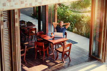 Freelance concept. Relaxed young bearded man working on laptop computer while sitting on terrace.