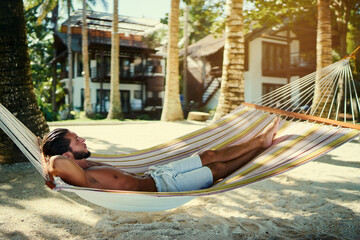 Tropical vacation. Young man relaxing on hammock in beach resort.