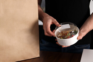 Man standing in the kitchen holds a container with food. Delivery healthy food home. Consumption, eating and people concept.