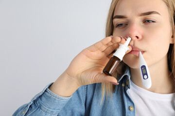 Woman with nasal drops and thermometer on light background, runny nose concept