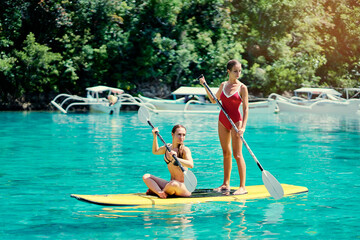 Summer holidays vacation travel. SUP Stand up paddle board. Young women sailing together on beautiful calm lagoon.