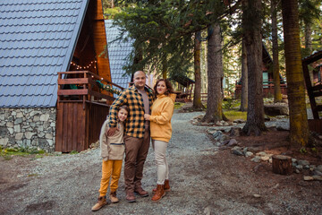 Happy family of travelers in the forest in the mountains near the wooden chalet house