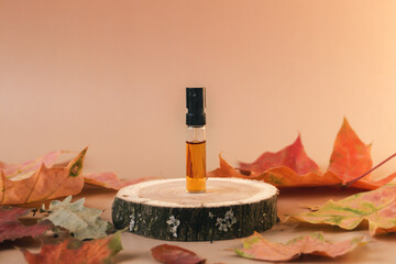 Glass perfume sample with brown liquid on a wooden tray standing on beige background with fallen leaves around. Luxury and natural autumn cosmetics presentation. Tester on a woodcut. Front view - obrazy, fototapety, plakaty