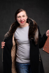 Happy fifty year old woman in a coat with a fur collar on a gray background. Portrait of a...