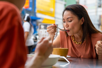 Group of Asian people friends tourist having dinner together at Chinatown street night market in Bangkok city, Thailand. Male and female friend enjoy outdoor lifestyle nightlife and eating street food