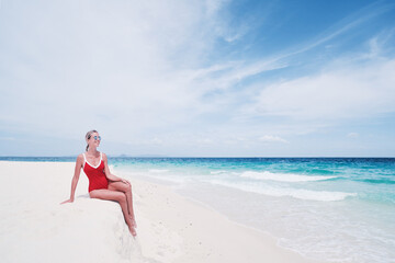 Vacation on the seashore.Young woman in red swimsuit sitting on the beautiful tropical white sand beach.